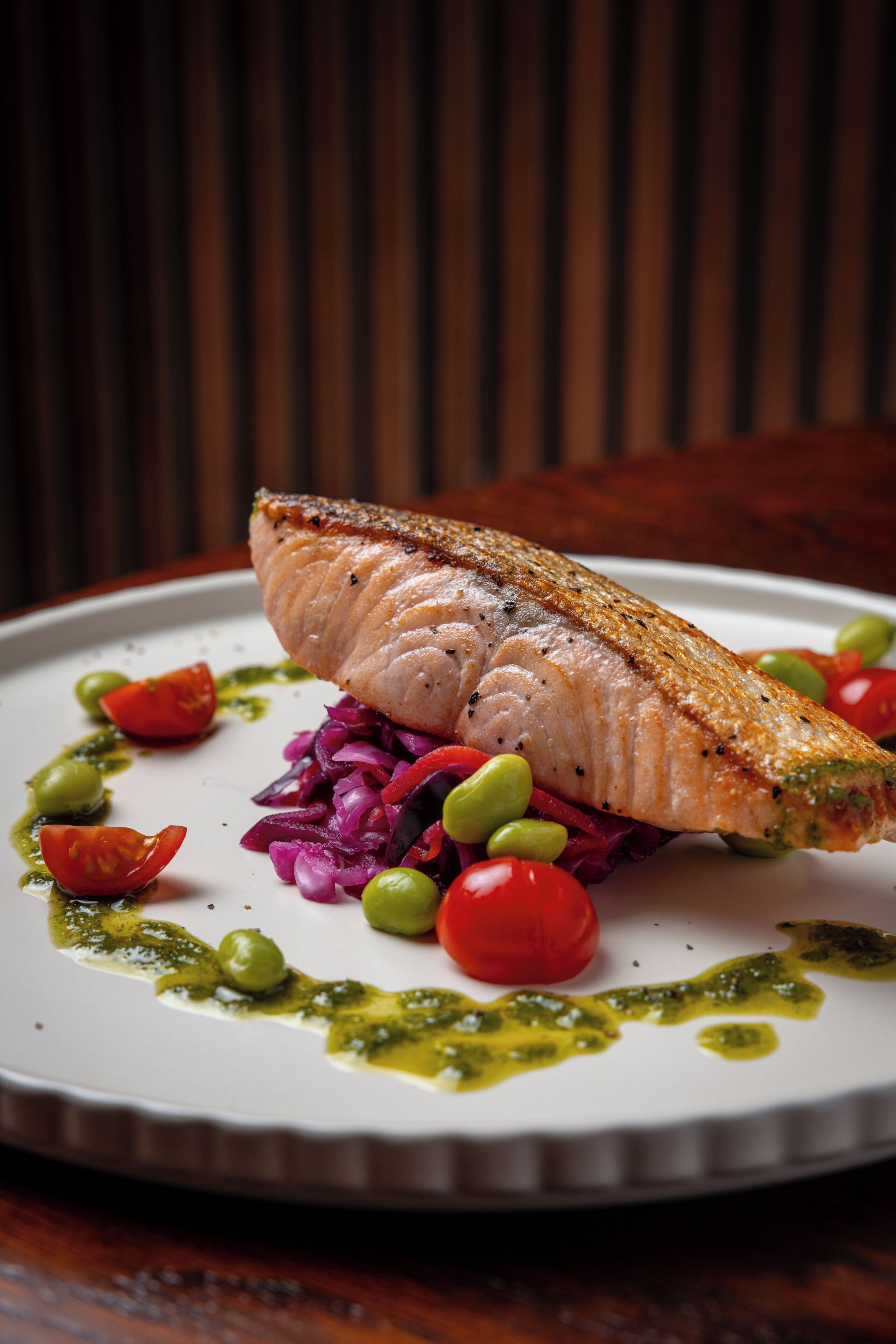 A plate with a fish fillet, tomatoes, and a green sauce.