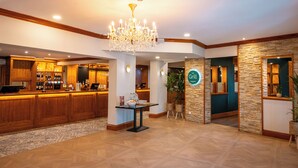 A hotel lobby with a reception desk, a chandelier, a bar area, and a sign for 'The Grill.'