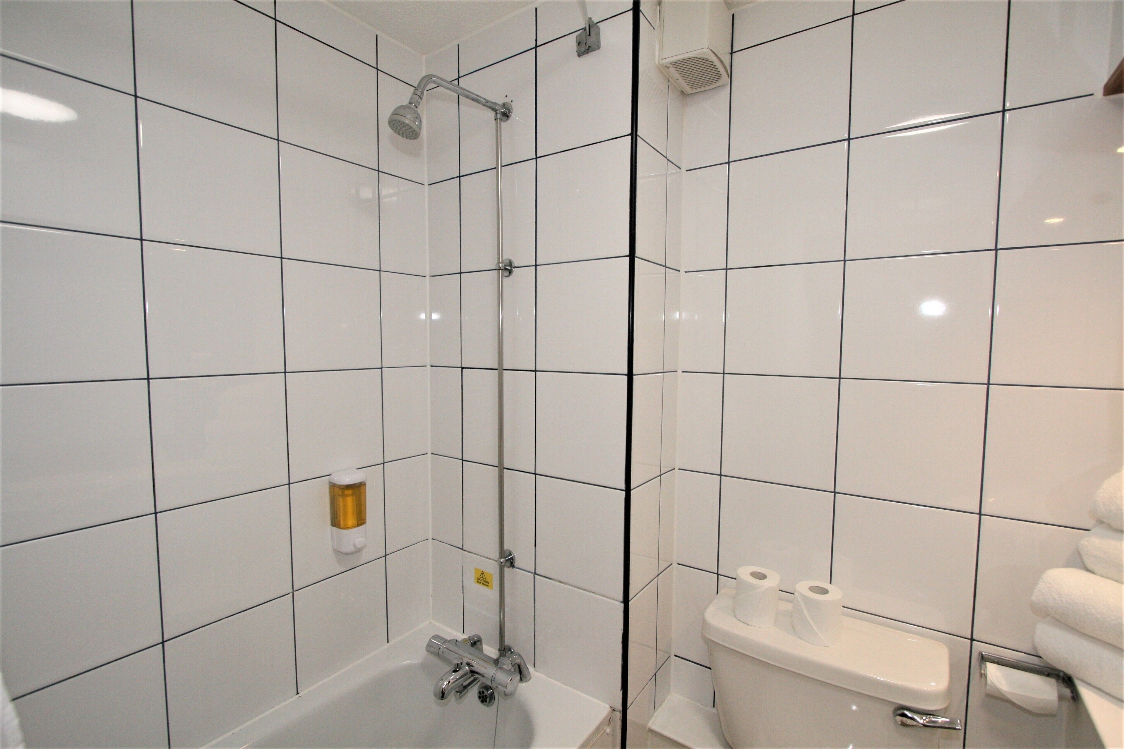 A bathroom with white tiles, a glass-enclosed shower, a toilet, and a towel rack.
