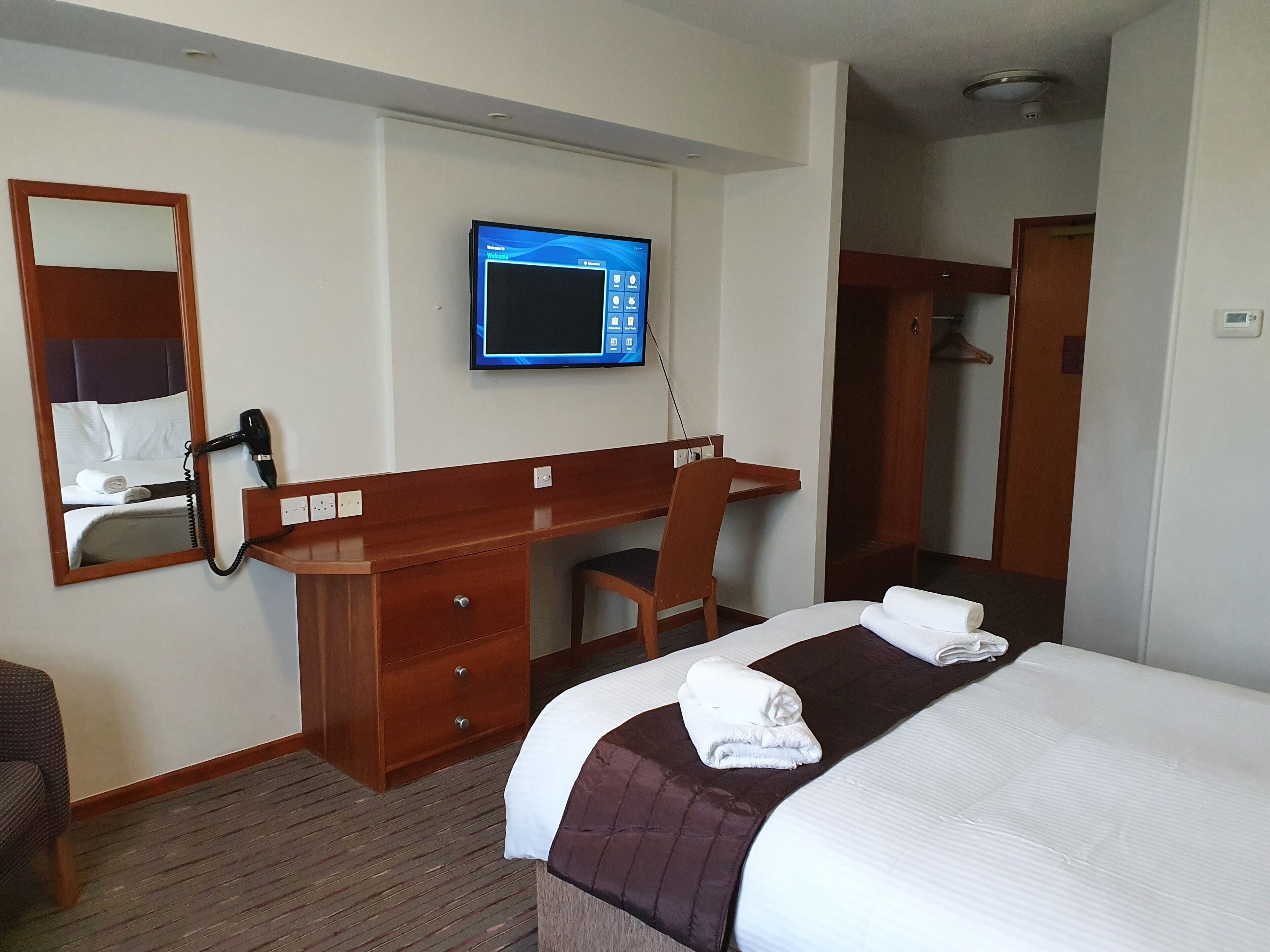 Une chambre d’hôtel équipée d’un lit, d’un bureau, d’une chaise, d’une télévision et d’un miroir.