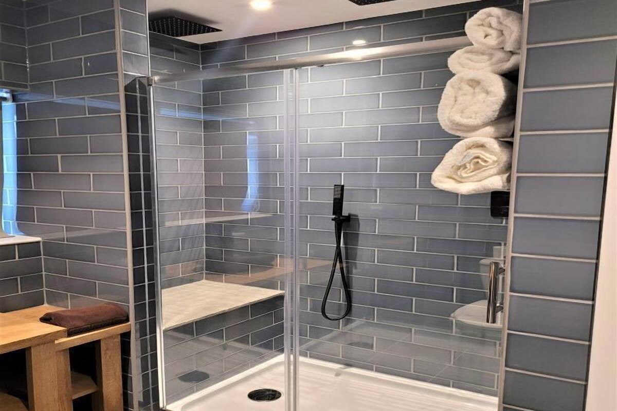 A modern shower with glass doors, a towel rack, and a wooden bench.