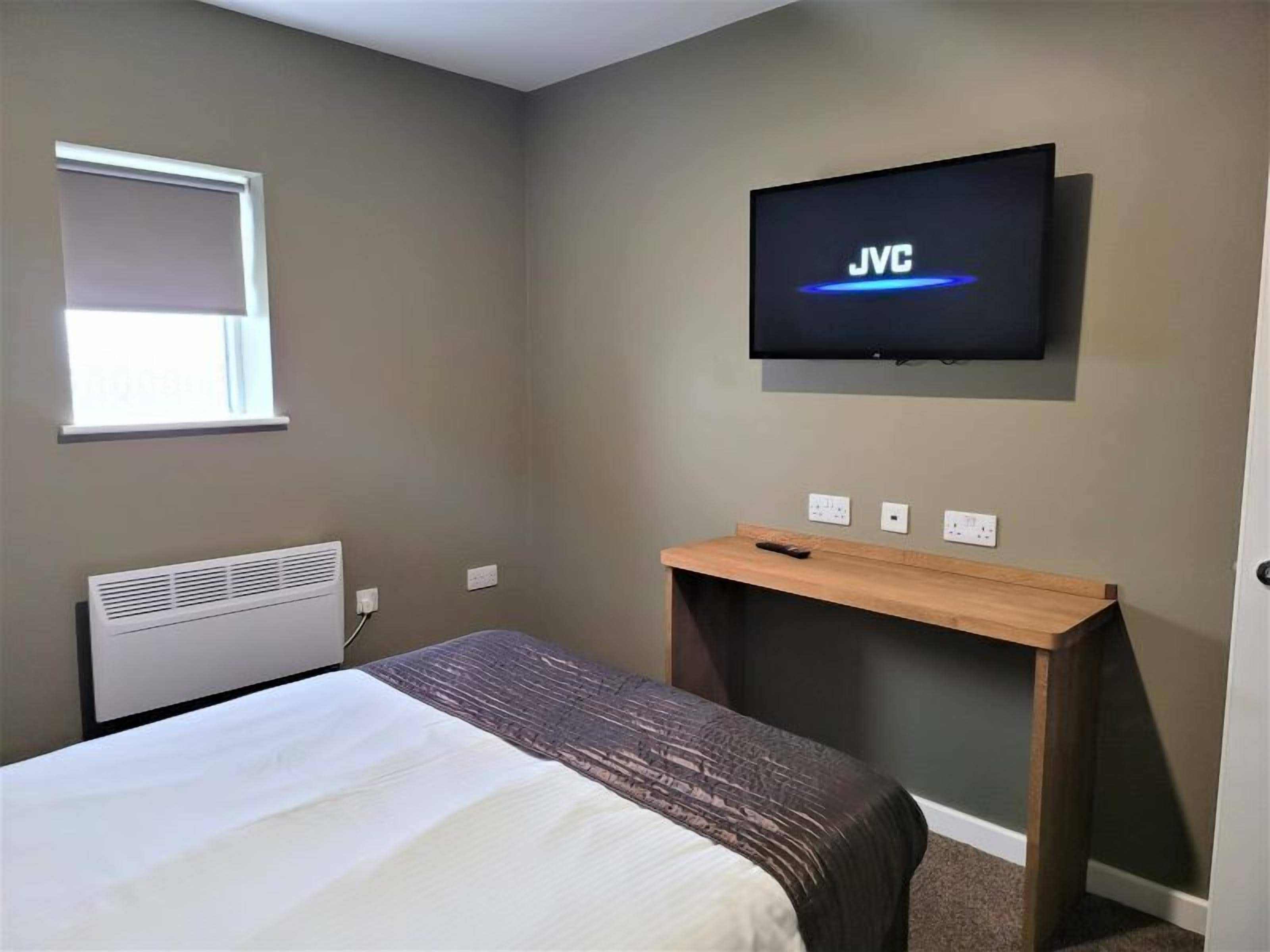Habitación de hotel con cama, televisor montado en la pared, ventana y escritorio.