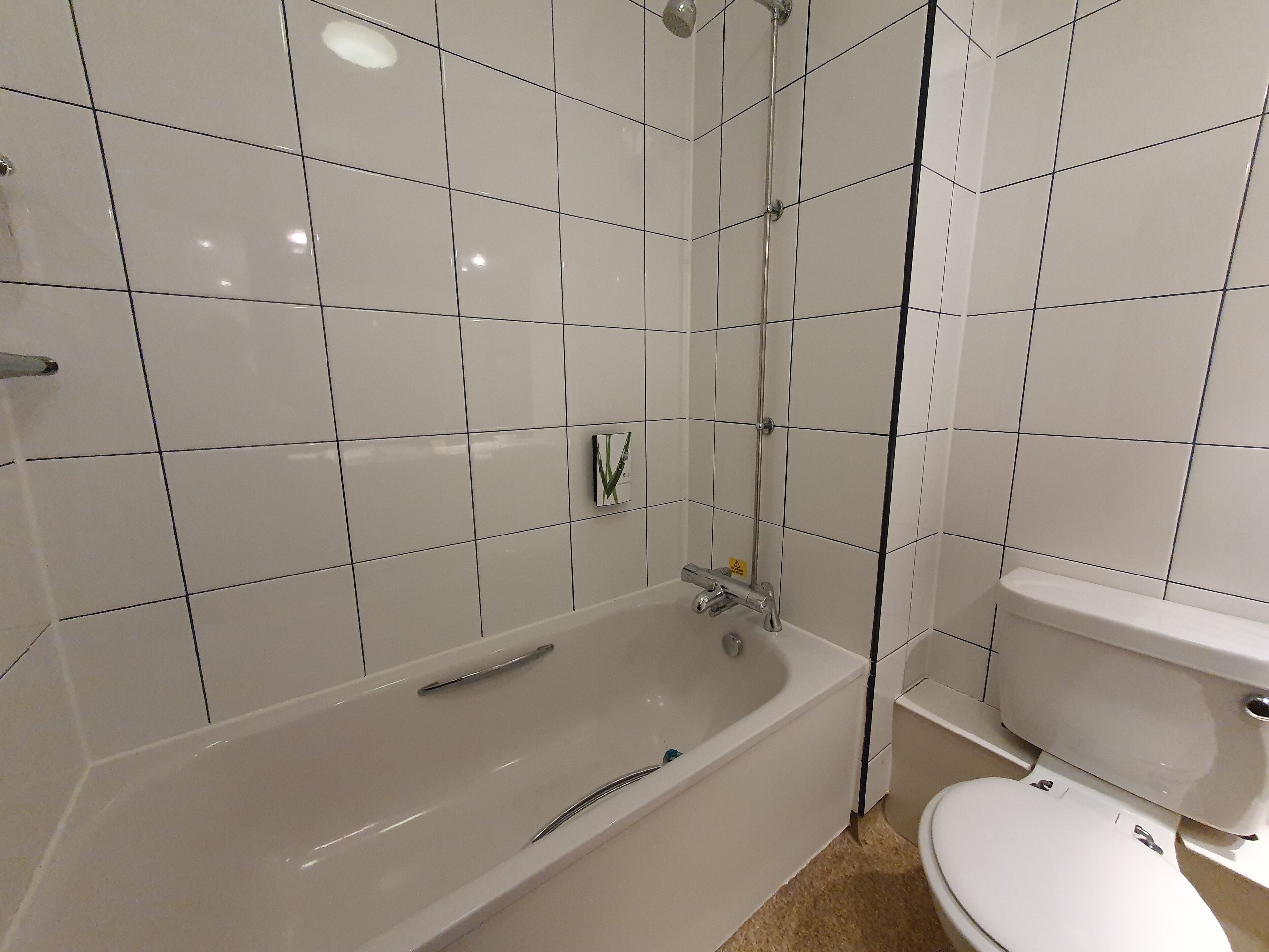 A bathroom with white tiles, a bathtub, and a toilet.
