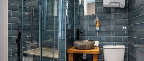 A modern bathroom with a glass-enclosed shower, a wooden vanity with a stone basin, a toilet, and a mirror above the sink.