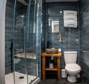 A modern bathroom with a glass-enclosed shower, a wooden vanity with a stone basin, a toilet, and a mirror above the sink. - The Oakwood Hotel (Gloucester)