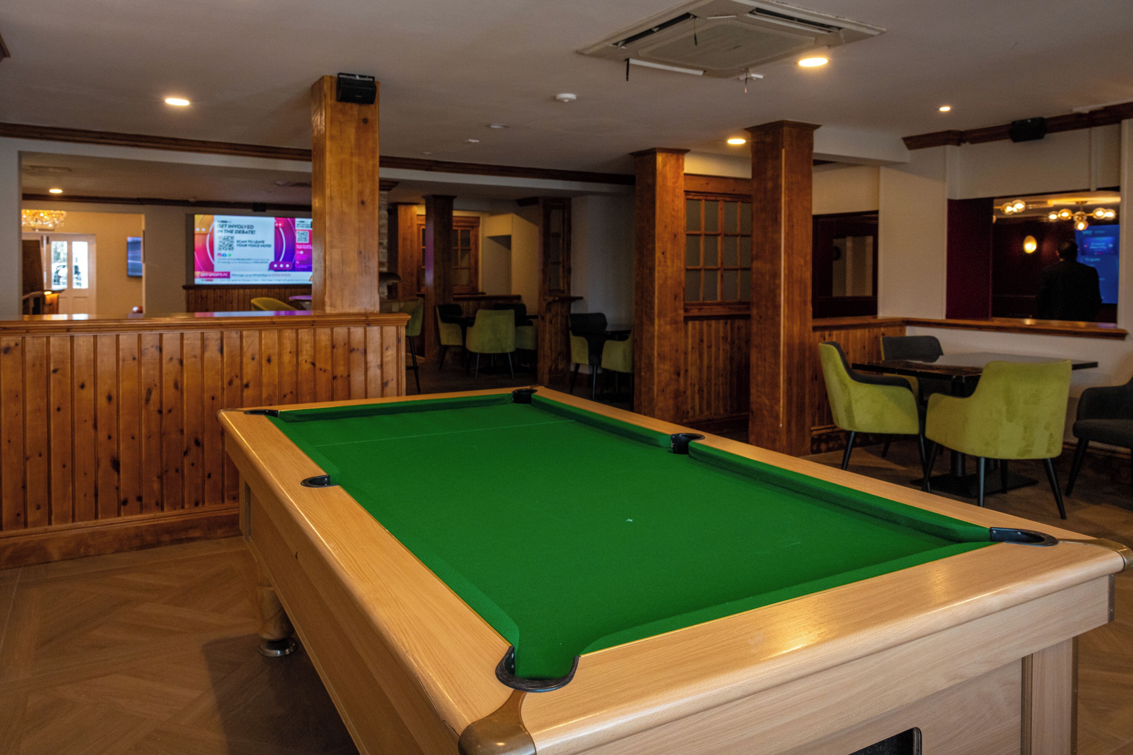 A pool table in a room with wooden walls and a bar area in the background.
