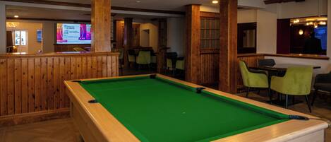 A pool table in a room with wooden walls and a bar area in the background.