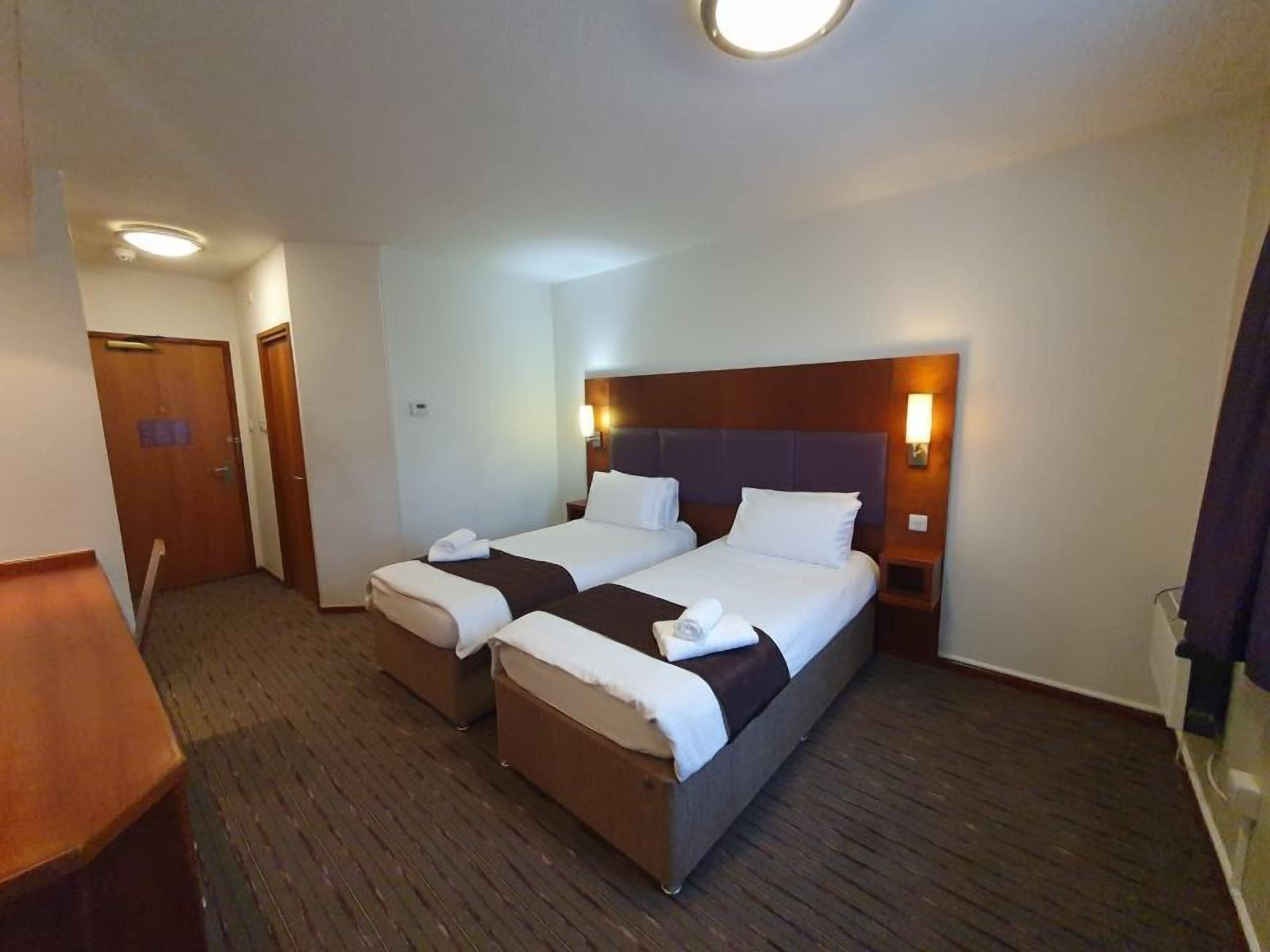 A hotel room with two beds, a wooden headboard, bedside lamps, and a carpeted floor.