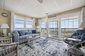 Ein Zimmer mit einem gestreiften Sofa, einem runden Couchtisch, Korbstühlen und Meerblick durch große Fenster.