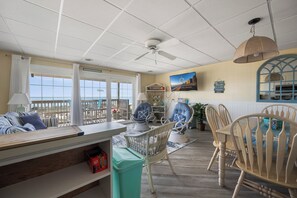 Ein Zimmer mit Meerblick, Korbmöbel, einem Esstisch und einem Deckenventilator.