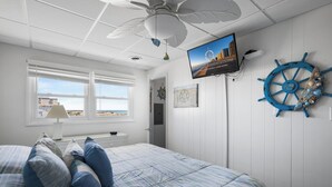 A bedroom with a bed, a television, a ceiling fan, a window, and a wall-mounted ship's wheel. - North OC, charming 2 bedroom oceanfront with Friday to Friday stay (Ocean City)