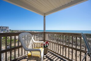 Ein Balkon mit Korbstuhl und Kissen, mit Blick auf einen Strand und freien Blick auf den Ozean.
