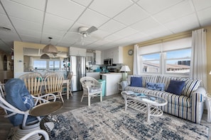 A spacious living area with a sofa, chairs, a coffee table, and a kitchen in the background.