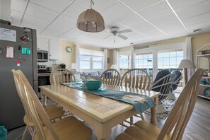 A dining area with a wooden table, chairs, a ceiling fan, and a view of the ocean.