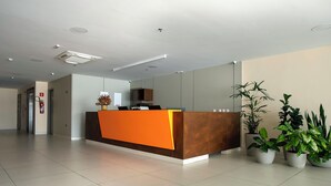 A modern reception desk with a brown and orange color scheme, surrounded by potted plants. - Verano Pajucara By Tropicalis (Maceió)