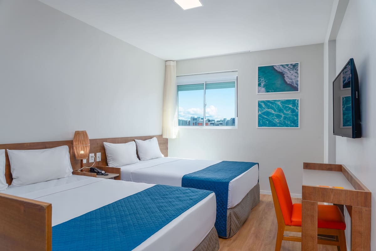 Ein Hotelzimmer mit zwei Betten, einem Schreibtisch, einem Stuhl und einem Fernseher.