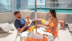 A rooftop terrace with a pool, white lounge chairs, and a table with a towel and sunglasses. - Verano Pajucara By Tropicalis (Maceió)