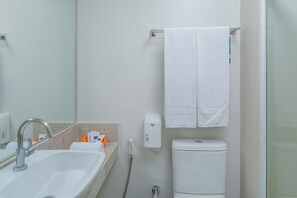 A bathroom with a sink, mirror, towel rack, toilet, and a handheld showerhead. - Verano Pajucara By Tropicalis (Maceió)