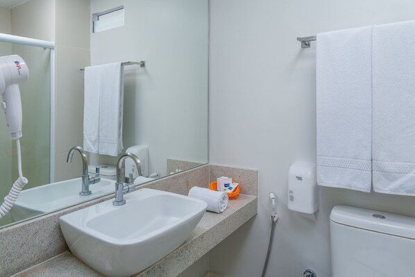 Un baño con lavamanos, espejo, toallero y secador de manos.