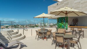 A rooftop terrace with outdoor seating, a bar, and a view of the cityscape. - Verano Pajucara By Tropicalis (Maceió)