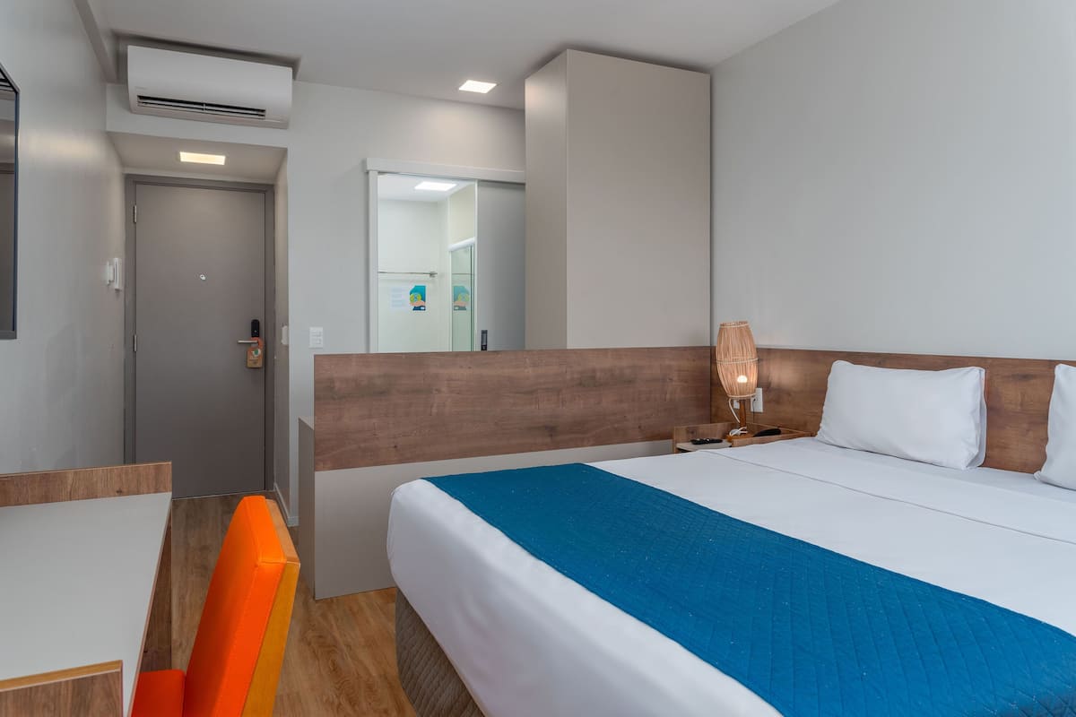 Ein Hotelzimmer mit Bett, Schreibtisch, Stuhl und einem durchgegangenen Tür sichtbaren Badezimmer.