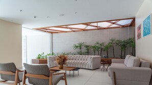 A modern living room with a sectional sofa, a coffee table, and two rocking chairs. There are several potted plants and a wooden ceiling structure. - Verano Pajucara By Tropicalis (Maceió)