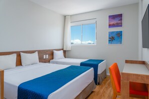 A hotel room with two beds, a desk, and a chair. There is a window with a view of the sky and clouds. - Verano Pajucara By Tropicalis (Maceió)