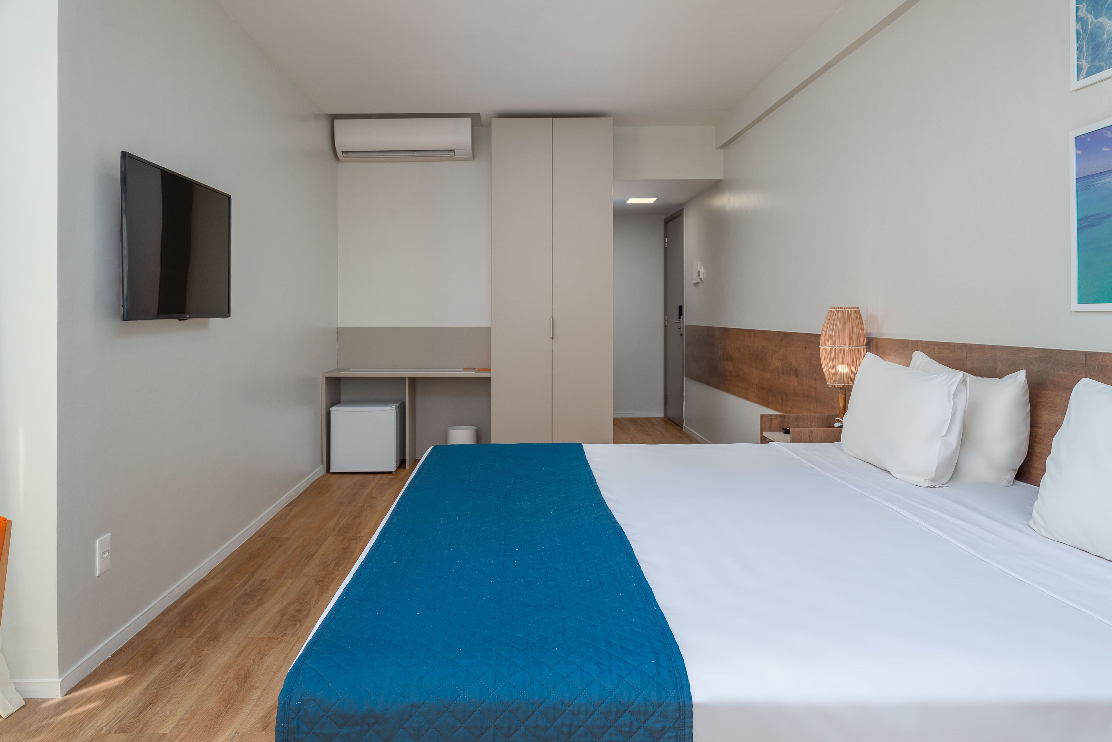 A hotel room with a bed, a TV, a desk, and a small kitchenette.