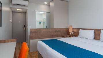 A hotel room with a bed, a desk, a chair, and a bathroom visible through an open door.