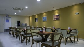 A dining area with multiple tables and chairs, a clock on the wall, and framed pictures on the wall. - Verano Pajucara By Tropicalis (Maceió)