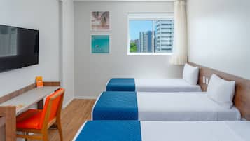 Habitación de hotel con cama, escritorio, silla, televisión y ventana con vista a la ciudad.