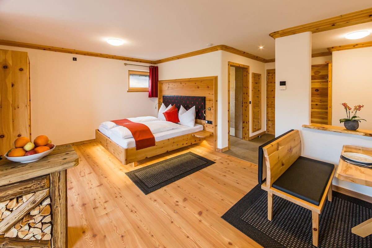 A wooden-floored room with a bed, a chair, and a small table.