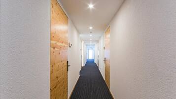 Un pasillo con puertas de madera y suelo alfombrado, que conduce a una habitación luminosa con ventana.