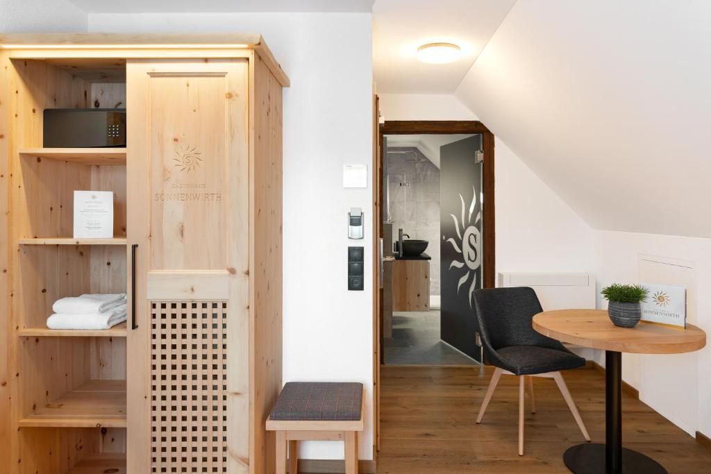 A wooden sauna room with a bench, a small table with a plant, and a wall-mounted sauna heater.