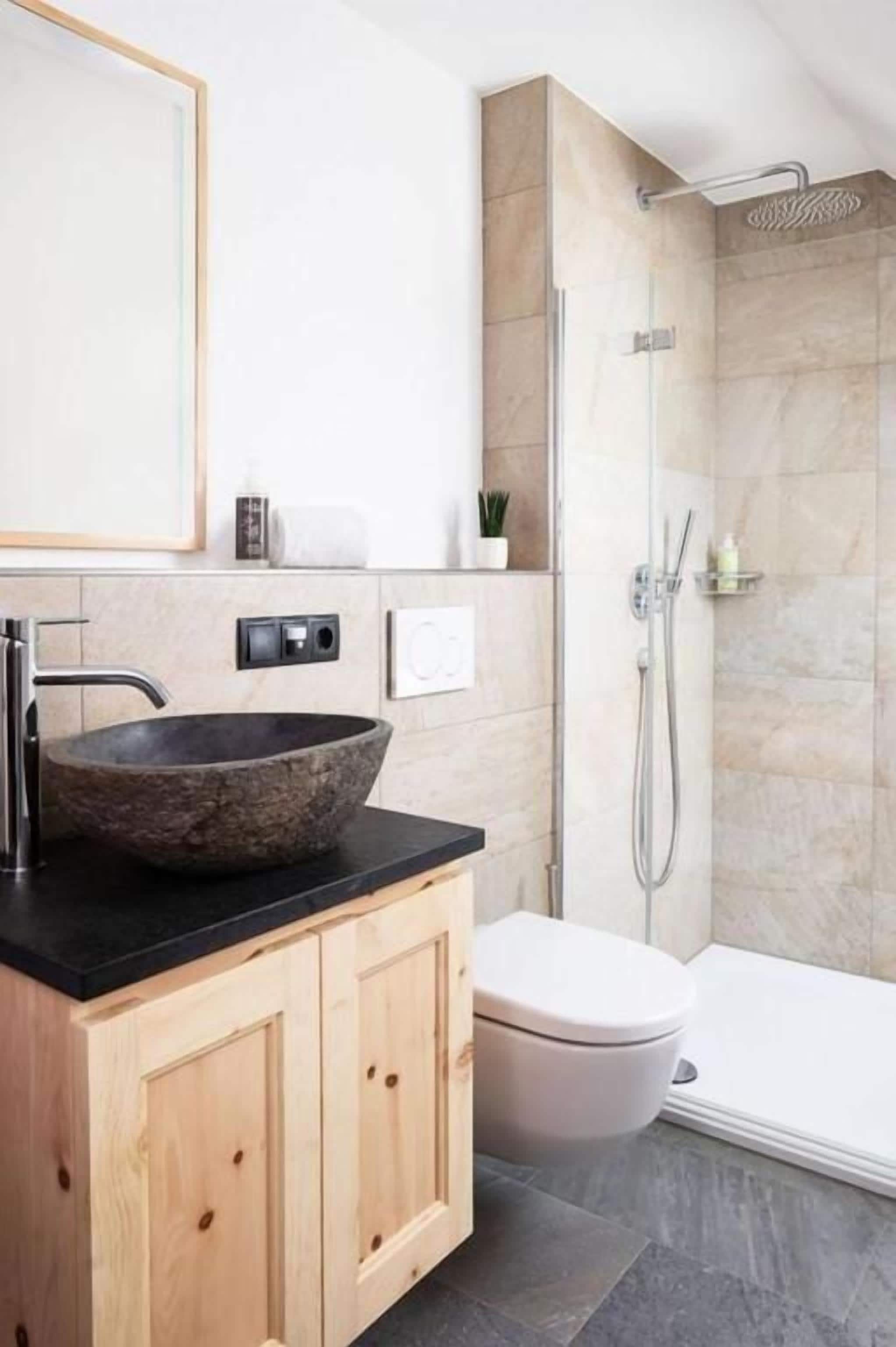 A modern bathroom with a stone sink, wooden cabinets, a toilet, and a glass shower enclosure.