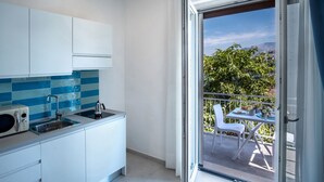 A modern kitchen with white cabinets and a blue-tiled backsplash, leading to a balcony with a table and chairs. - Family Apartment in Sorrento Centre (Sorrento)