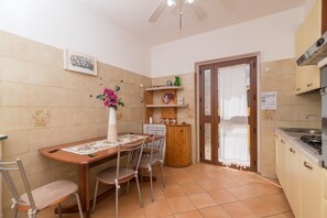 A compact kitchen with a dining table, chairs, a small cabinet, and a door leading to another room.