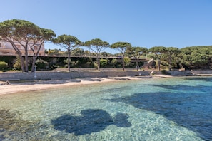 A coastal scene with clear water, trees, and a building in the background.