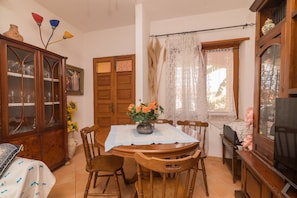A dining area with a wooden table, chairs, a vase with flowers, a cabinet, and a window with curtains.
