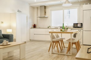 A modern kitchen with white cabinetry, a dining table with chairs, a microwave, and a refrigerator.