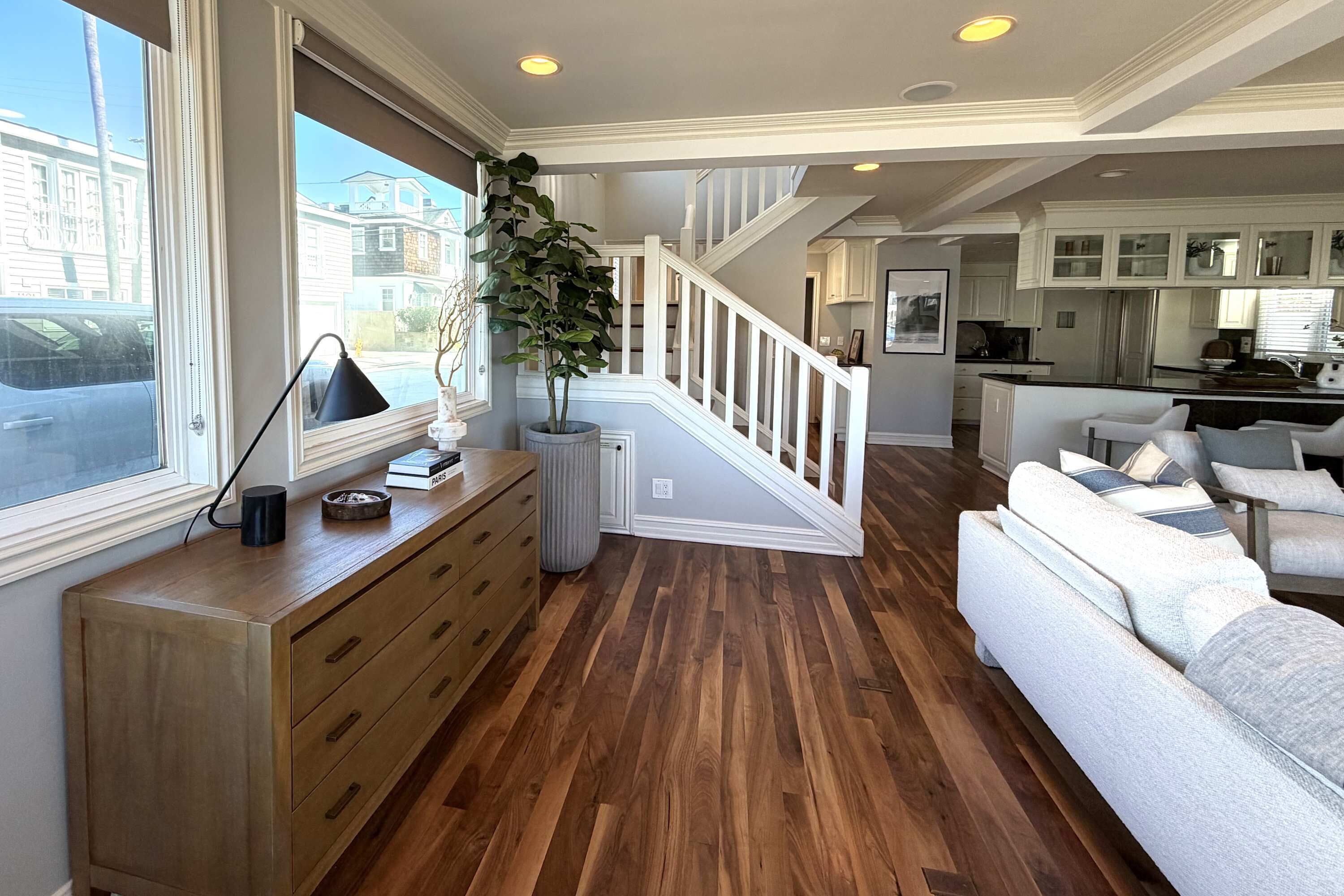 A spacious living area with hardwood flooring, a white sofa, a wooden cabinet, and a staircase leading to a kitchen.