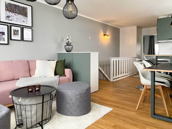 Ein modernes Wohnzimmer mit einer Couch, einem Hocker, einem runden Tisch und einem Essbereich mit Stühlen und einem Tisch.