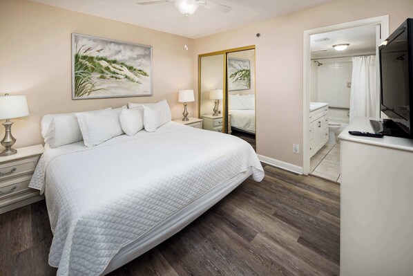 A bedroom with a large bed, bedside tables, a TV, and a bathroom visible through an open door.