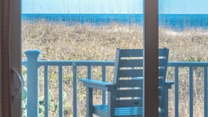 Vista desde un porche con una silla, con vista a una playa con pastos altos y el océano.