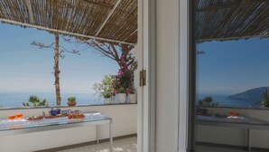 Un balcón con una mesa dispuesta para el desayuno, vista al mar y una pérgola en la parte superior.