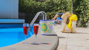 Escena junto a la piscina con dos copas de vino tinto, una jarrón decorativo y un bolso con un lazo amarillo.