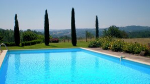Ein rechteckiger Swimmingpool mit klarem, blauem Wasser, umgeben von gepflegter Vegetation und hohen Zypressen.