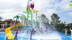 Ein Wasserpark mit einer gelben Rutsche, mehreren Wasserstrahlern und einem Poolbereich.