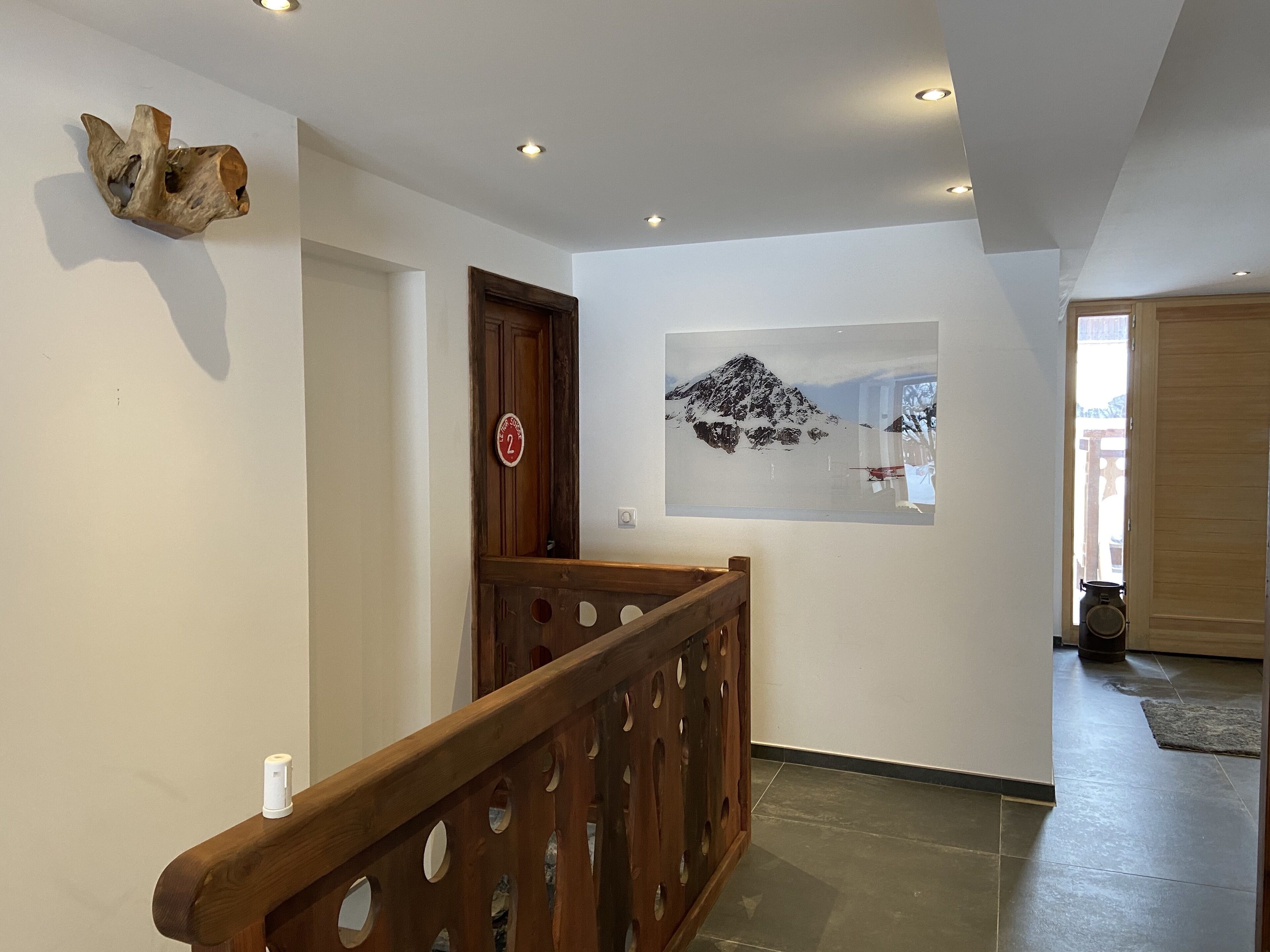 A hallway with a wooden railing, a wall-mounted sculpture, and a framed picture of a mountain.