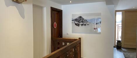 A hallway with a wooden railing, a wall-mounted sculpture, and a framed picture of a mountain.